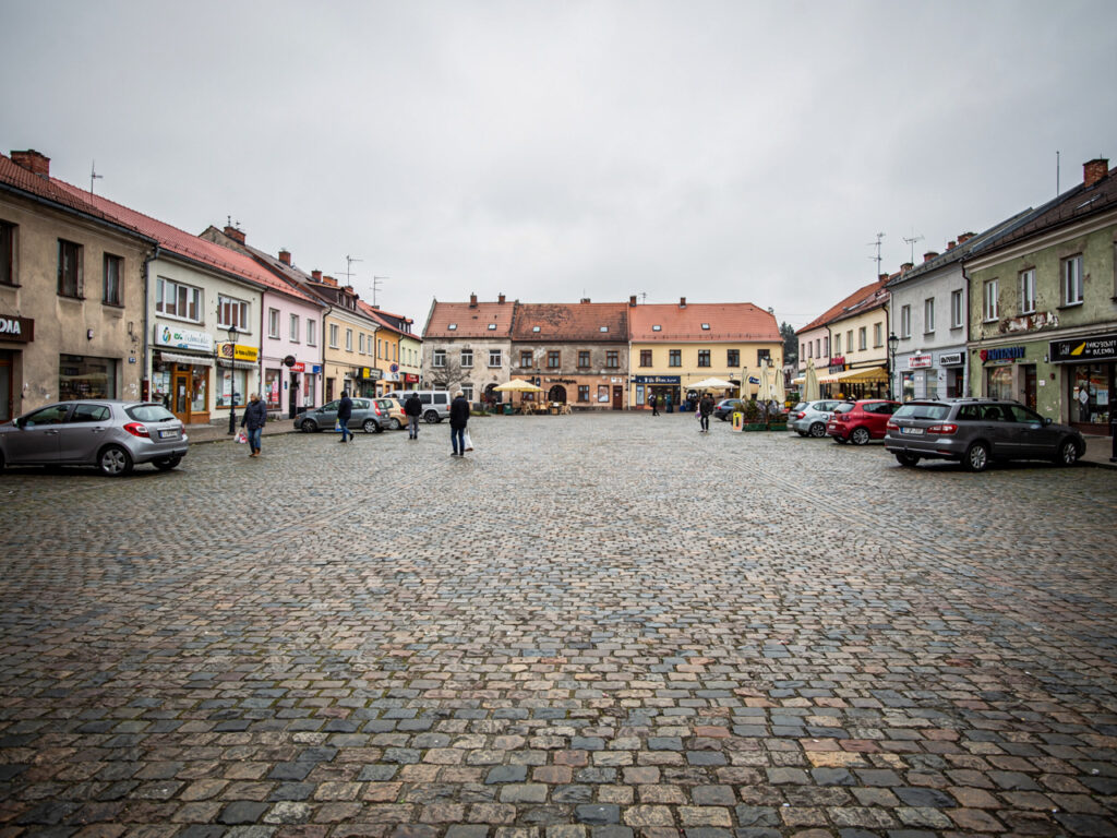 Rynek małego polskiego miasta z niską zabudową i nielicznymi przechodniami, pochmurne naturalne światło